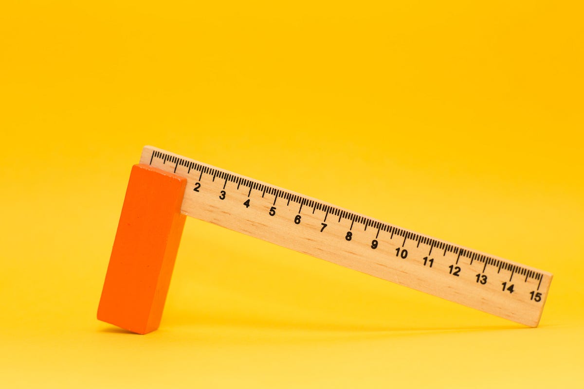A ruler with one end leaning on an orange block with a yellow background.